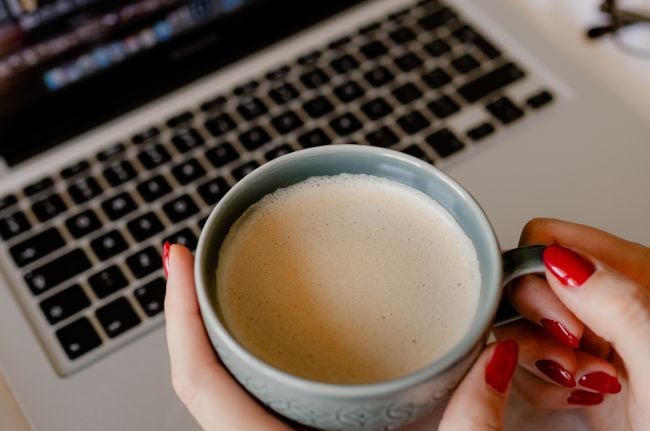 woman holding a cup of coffee in front of a laptop computer