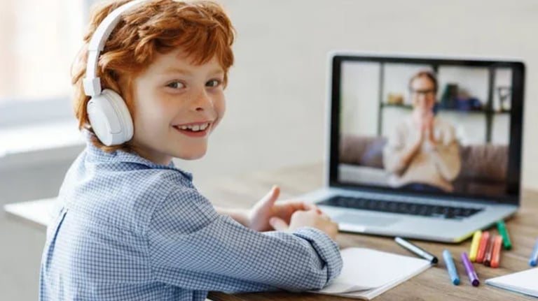 a young boy with headphones and a laptop, on the screen you can see his language tutor, both smiling