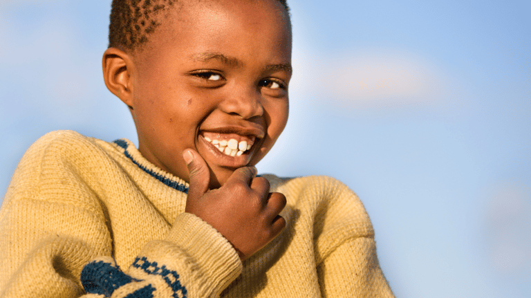 a young boy smiling and holding his hand up to his chin