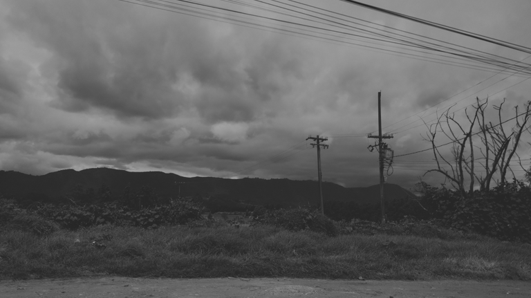 Paisaje monocromo de montañas bajo un cielo nublado con postes de luz.