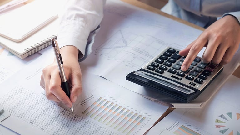 Partial view of an individual calculating and writing on a financial report or chart.