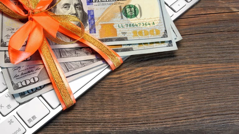 Partial view of hundred dollar bills resting on a computer keyboard.