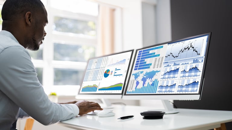 a man sitting at a desk with two monitors and a laptop