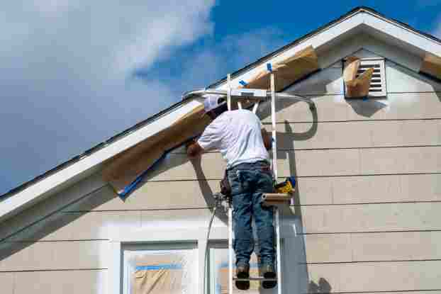 a man on a ladder painting a house with a sprayer