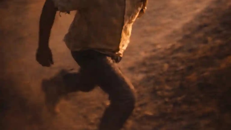 Indian man running on a rough road carrying a heavy load, motion blur showing urgency, struggle and burden.