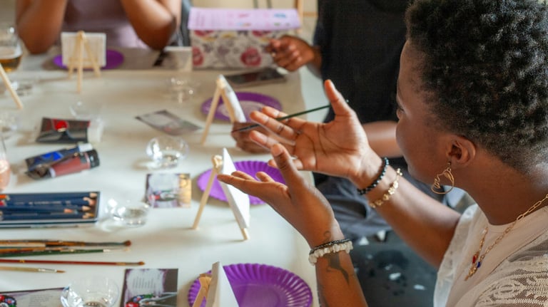 Group of people painting at a table with easels, brushes, and supplies — a creative, social activity