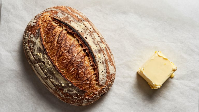 A flat lay of artisanal sourdough bread and fresh butter on a crisp parchment background, styled for a North American / US bakery brand.