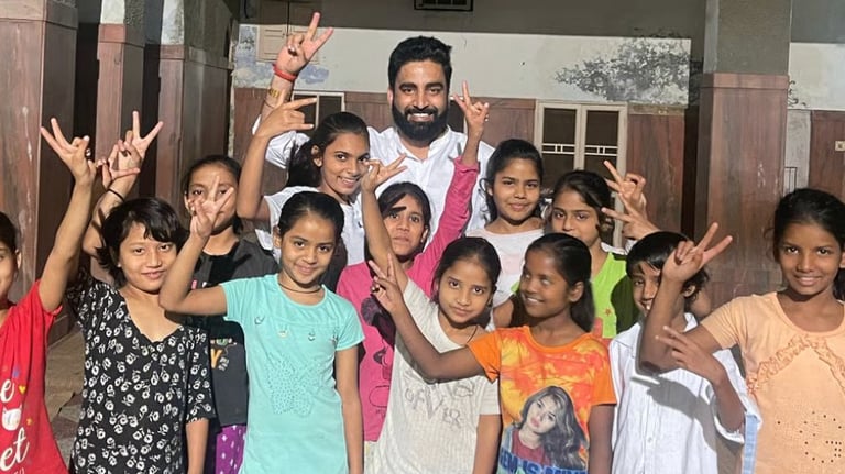 Vikash Sharma with a group of cheerful young girls making peace signs at a school or community center