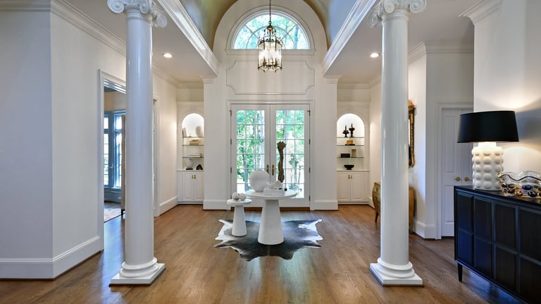 Elegant luxury home foyer featuring white ionic columns, vaulted ceilings, and a large arched window above the glass entry
