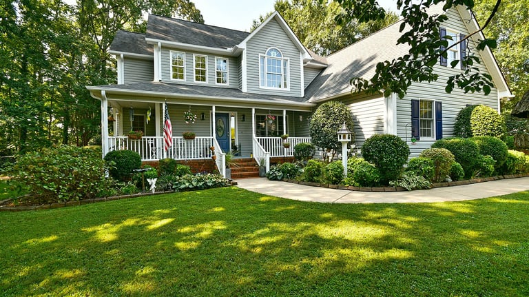 Two-story grey traditional home with white trim, a large front porch, and lush green lawn.