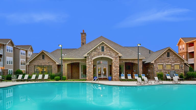 Luxury apartment complex outdoor swimming pool and stone clubhouse with lounge chairs.