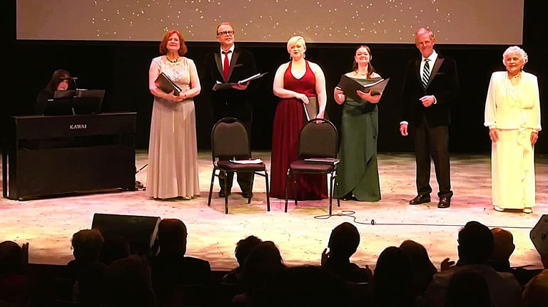 Singers in formal attire performing a vocal concert on stage with a piano accompanist.