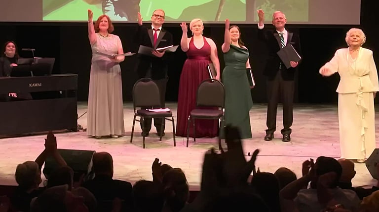 A group of singers in formal attire taking a bow on stage a the end of a live musical performance.
