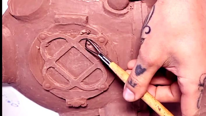 Close up of a hand holding a sculpting tool, carving a Mark 5 diving helmet out of clay.  This sculpture was a commission. 
