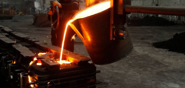 Stock image of a foundry - A pot of glowing melted bronze being poured into a mold.