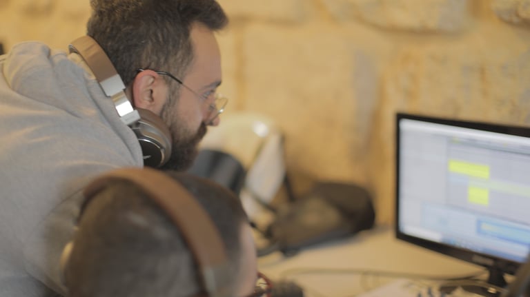 a man with headphones and a student on the computer learning music production