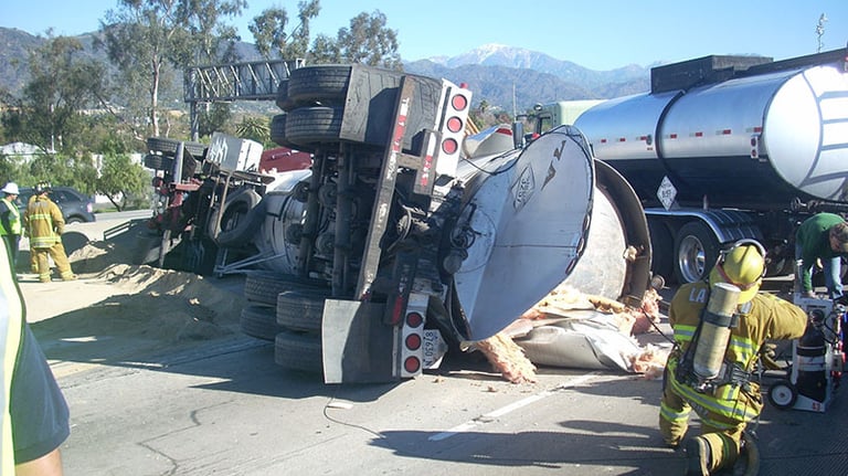 a firefighter standing next to a fallen chemical truck with a hose attached to it