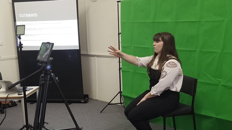 Laura sits in front of a greenscreen and in front of an ipad teaching a class about cutaways