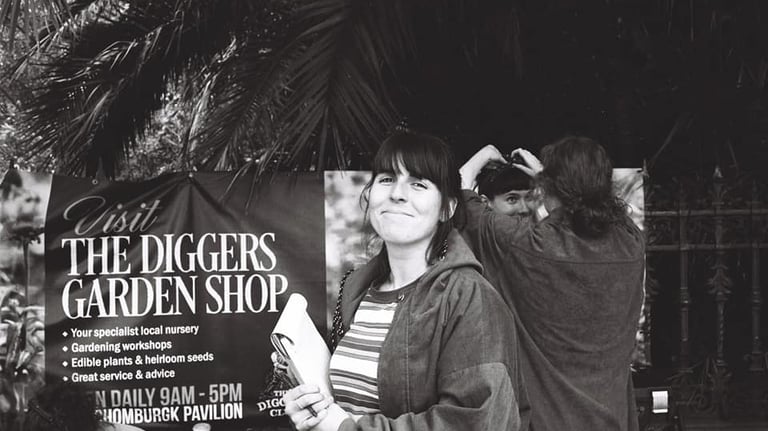 A black and white 35mm photo of Laura holding a clipboard. Smiling on set as actors fix their hair