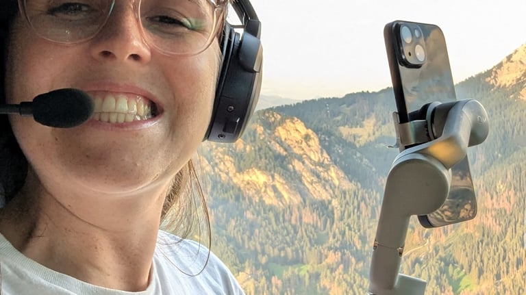 Laura sits in a helicopter over the Italian Dolomites, holding a phone in a gimbol. 