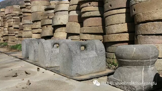 Ancient Chinese stone strength training equipment and stacked millstones at a Shaolin martial arts temple.