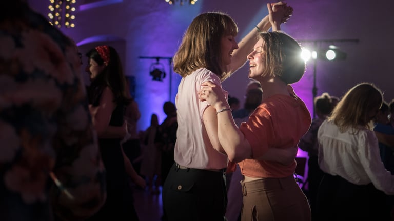Two women smiling and dancing together at a lively party with purple event lighting.