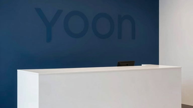 A minimalist photo of a sleek white reception area with a deep blue accent wall, featuring a subtle YOON logo, South Asian / Pakistani interior style, clean Apple-like aesthetics.