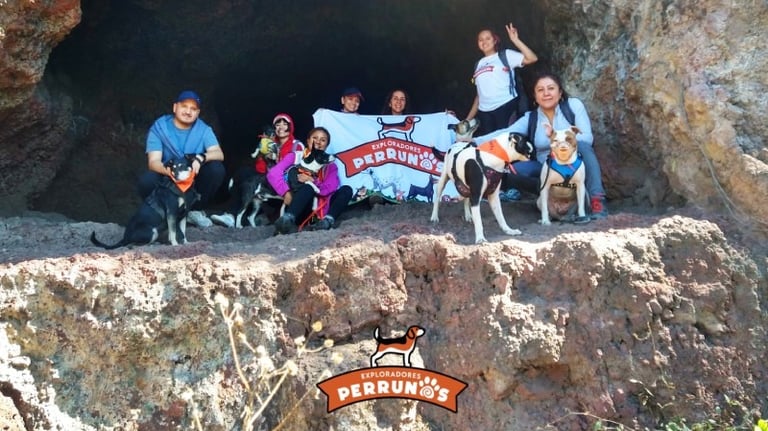 Un grupo de excursionistas con sus perros posando a las afueras de una cueva rocosa