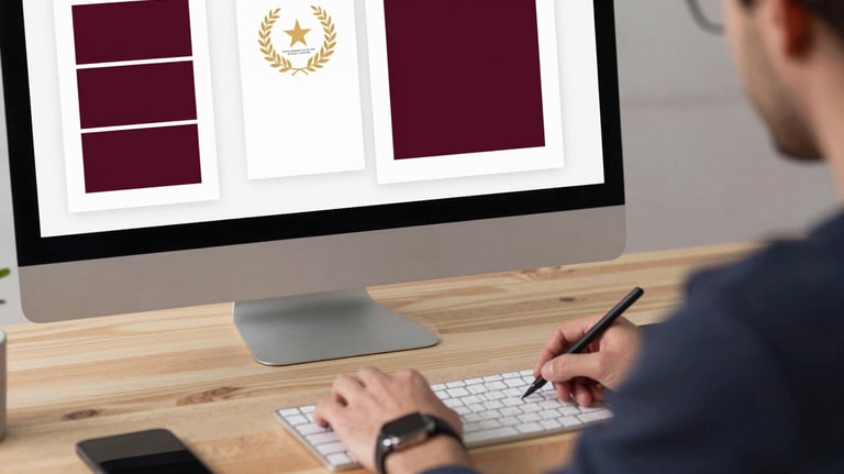 A professional designer at a clean wooden desk, working on a book cover layout on a large monitor. A mood board with deep ripe crimson swatches is visible.