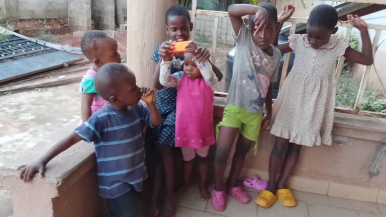A group of six young African children playing together and posing on a porch.