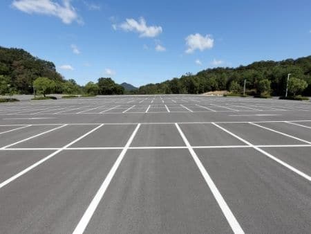 Empty asphalt parking lot with white painted lines under a blue sky with hills.