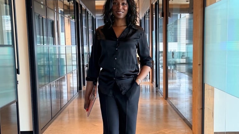 Ain in a black business suit walking through a modern glass-walled office hallway.