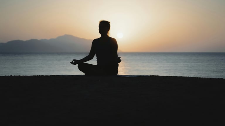 a meditating person sitting on a beach with a sunset in the background