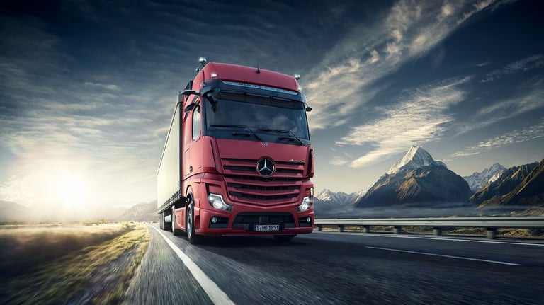 a red truck driving down a road with mountains in the background