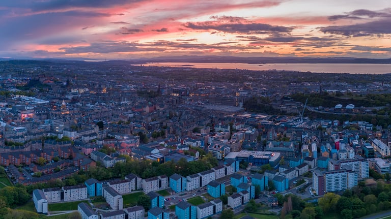 Aerial view of Edinburgh at dusk with dramatic pink sky over the city and Firth of Forth beyond
