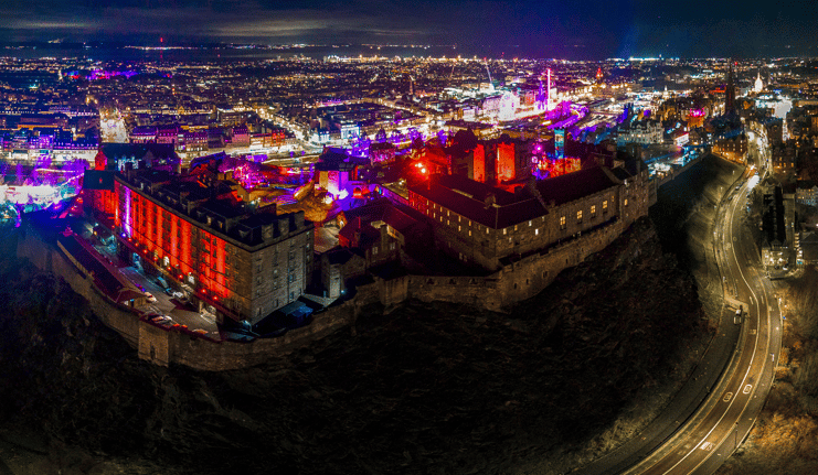 Aerial night view of Edinburgh Castle with colourful festival lights across the city and Princes Street