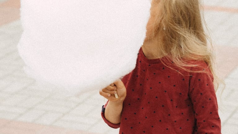 a girl in a red shirt eating a cotton candy cone that is bigger than her head