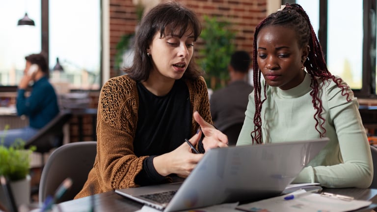 two women sitting at a table with laptops