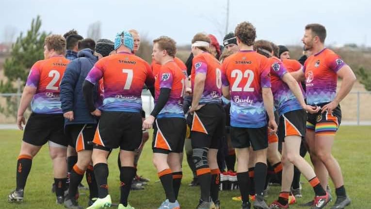 a group of rugby players huddle around a field during their tournament