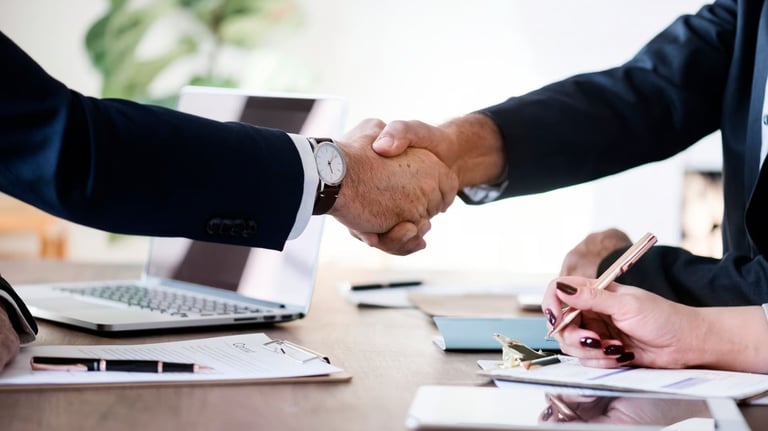 two people shaking hands over a desk with laptops