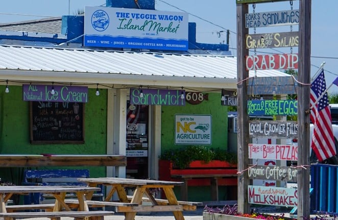 Exterior of The Veggie Wagon local island market with picnic tables and a signs for sandwiches and ice cream.