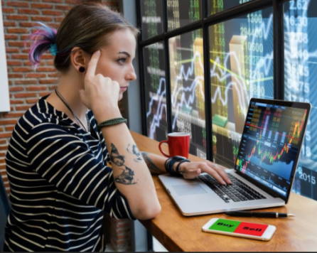 Mulher sentada a frente de computador com gráficos da bolsa de valores
