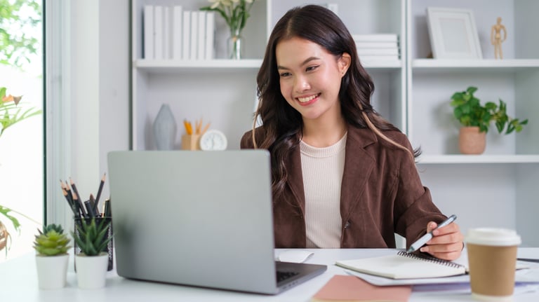 Chica sonriente sentada en un escritorio con un ordenador portátil y una libreta