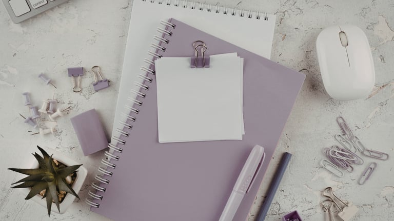 Flat lay of purple office supplies including spiral notebooks, a white mouse, and stationery on a desk.