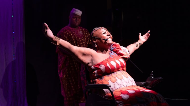 Fotografia de cena teatral com a artista Mona Rikumbi. Mulher negra, usuária de cadeira de rodas 