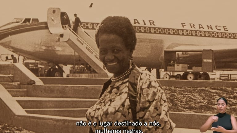Captura de vídeo da exposição de Carolina Maria de Jesus sorrindo em frente a um avião da AIR France