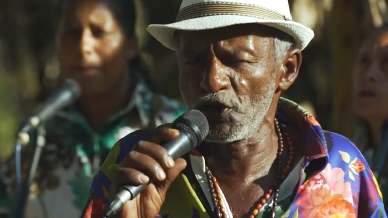 Foto de homem negro idoso cantando em um grupo de samba de coco.