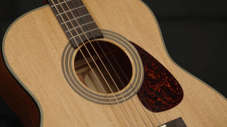 A close-up of the body of a classical acoustic guitar made of golden tan cedar wood, with intricate rosette details around the soundhole.
