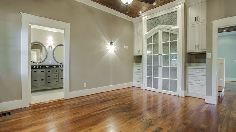 Elegant room with reclaimed wood floors, a ceiling fan, and white built-in cabinets near a bathroom.