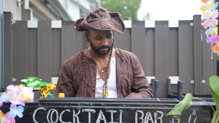 A male bartender in a pirate costume works at an outdoor tiki cocktail bar for a themed party.